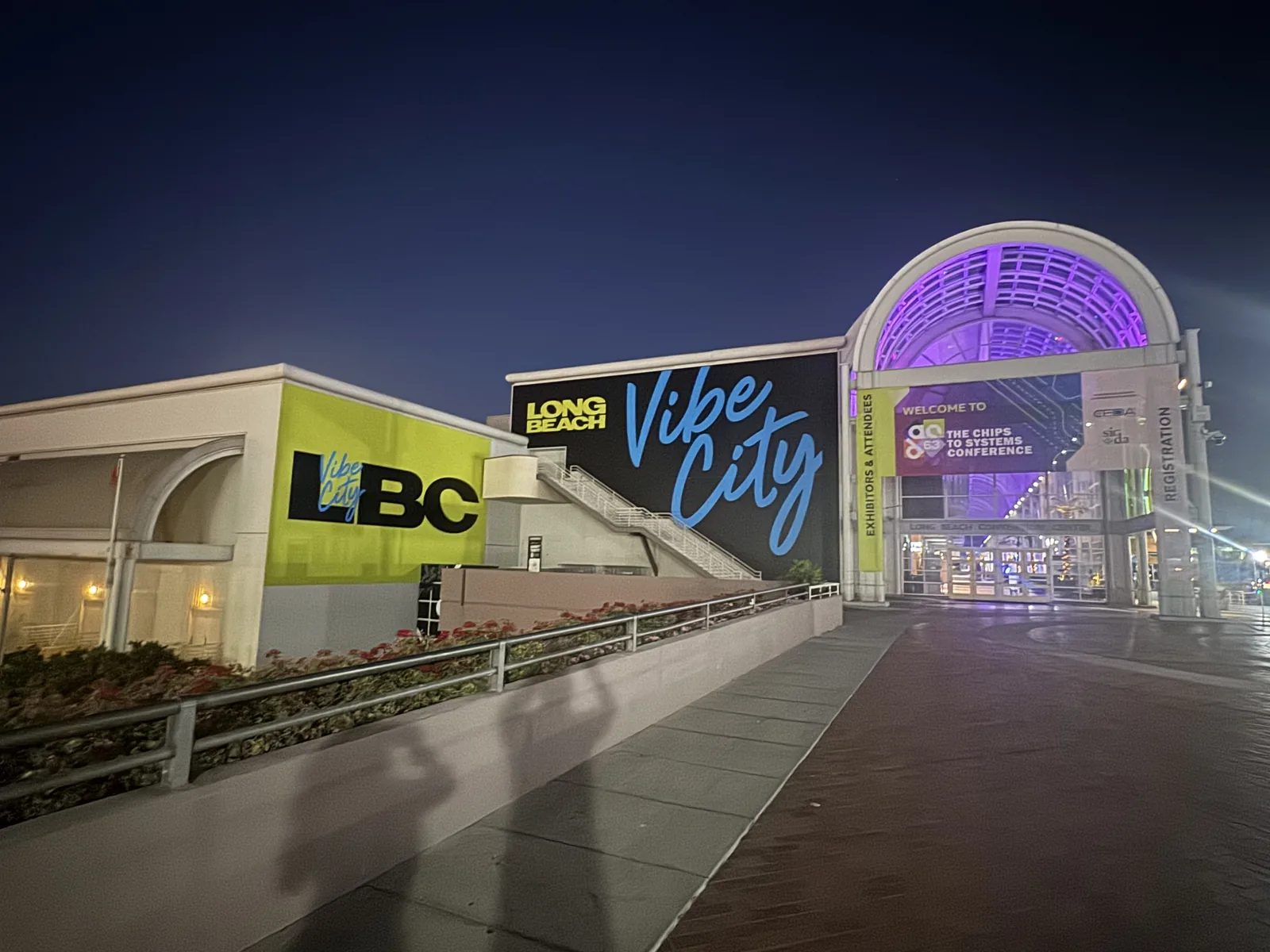 The Long Beach Convention Center at dusk. A large Vibe City mural fills the wall, and the lit entrance arch beyond it carries a DAC 63 welcome banner reading The Chips to Systems Conference.